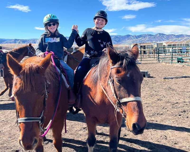 Girls holding hands while learning to ride horses